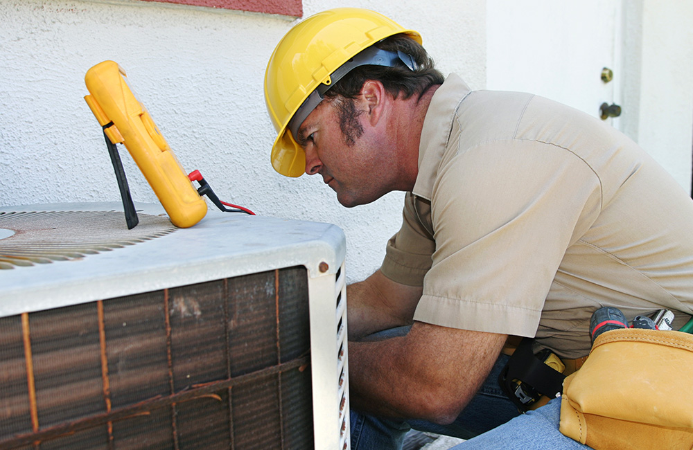 Reckingers Heating & Cooling HVAC tech repairing an air conditioning unit outside house